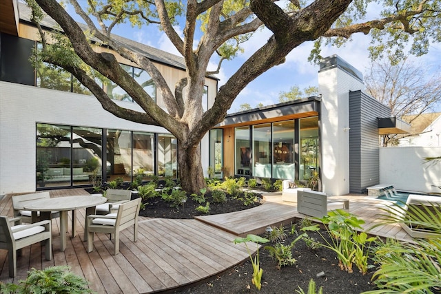 rear view of property with a deck, outdoor dining area, a chimney, and fence