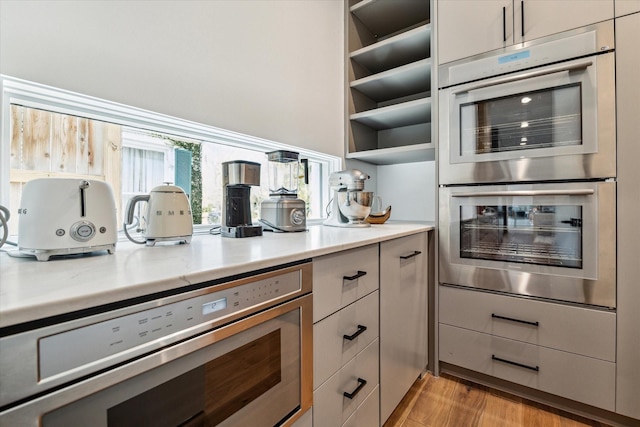 kitchen with light wood-style flooring, light countertops, appliances with stainless steel finishes, open shelves, and modern cabinets