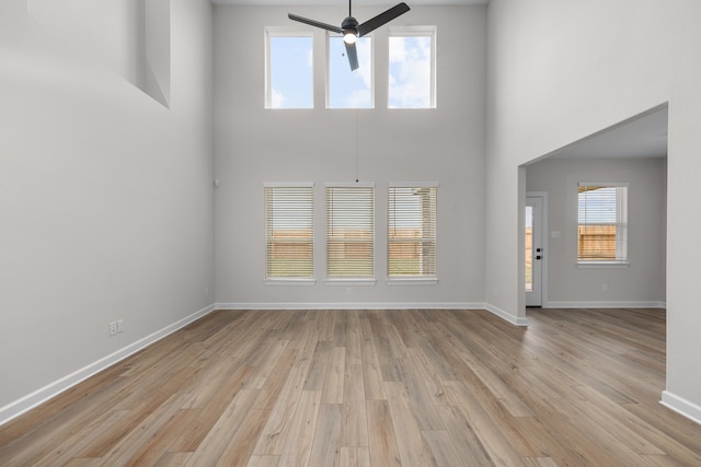 unfurnished living room featuring baseboards, a towering ceiling, a ceiling fan, and light wood-style floors