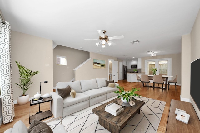 living area with light wood-type flooring, visible vents, baseboards, and ceiling fan