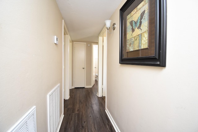 corridor with baseboards, visible vents, and dark wood-type flooring