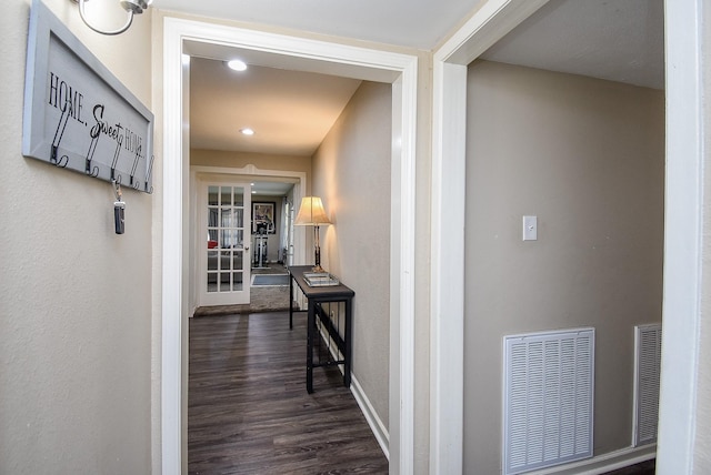 hall with dark wood-style flooring, visible vents, and baseboards