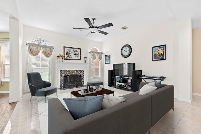 living area featuring light tile patterned flooring, a fireplace, visible vents, baseboards, and a ceiling fan