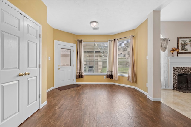 unfurnished dining area featuring a stone fireplace, dark wood-type flooring, visible vents, and baseboards