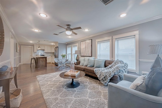 living area featuring recessed lighting, wood finished floors, a ceiling fan, visible vents, and crown molding