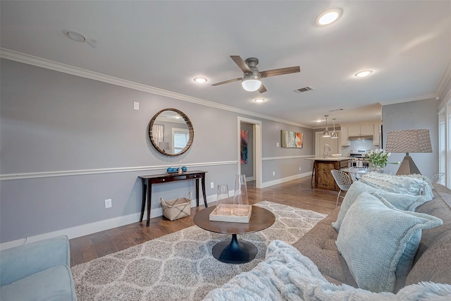 living area with baseboards, wood finished floors, visible vents, and crown molding