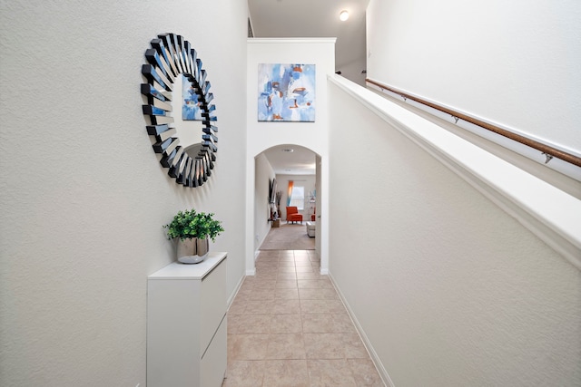 hall with arched walkways, baseboards, and light tile patterned floors