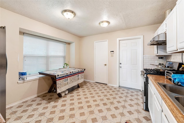 kitchen with tasteful backsplash, wooden counters, white cabinets, under cabinet range hood, and stainless steel gas range oven