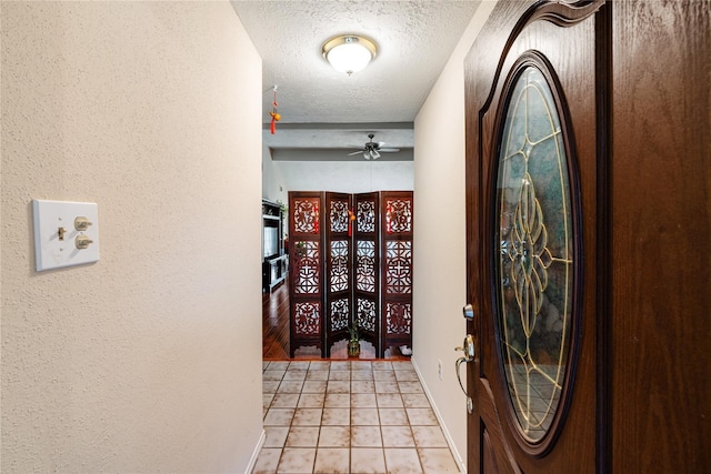 entrance foyer featuring a textured wall, a textured ceiling, baseboards, and light tile patterned floors