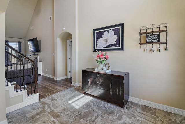 interior space with arched walkways, high vaulted ceiling, stairway, and baseboards