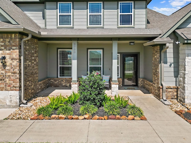 doorway to property featuring covered porch, brick siding, and a shingled roof