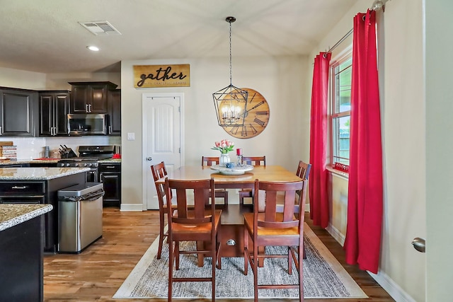 dining area featuring a chandelier, light wood finished floors, visible vents, and baseboards