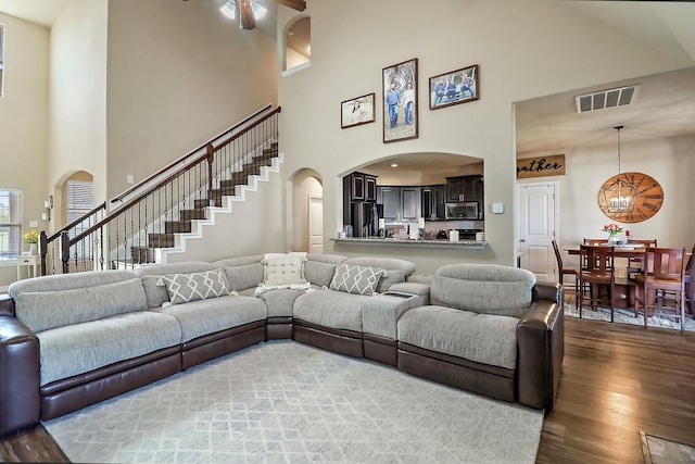 living area with visible vents, arched walkways, stairway, wood finished floors, and ceiling fan with notable chandelier