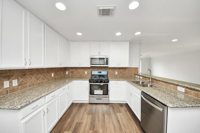 kitchen featuring stainless steel appliances, visible vents, white cabinets, a sink, and a peninsula