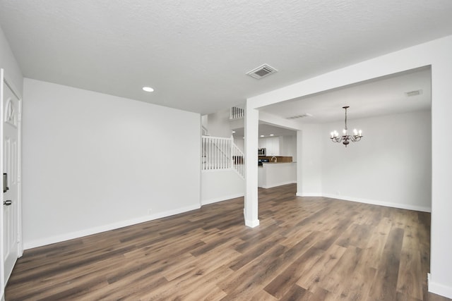 unfurnished living room with a textured ceiling, dark wood-type flooring, baseboards, stairway, and an inviting chandelier