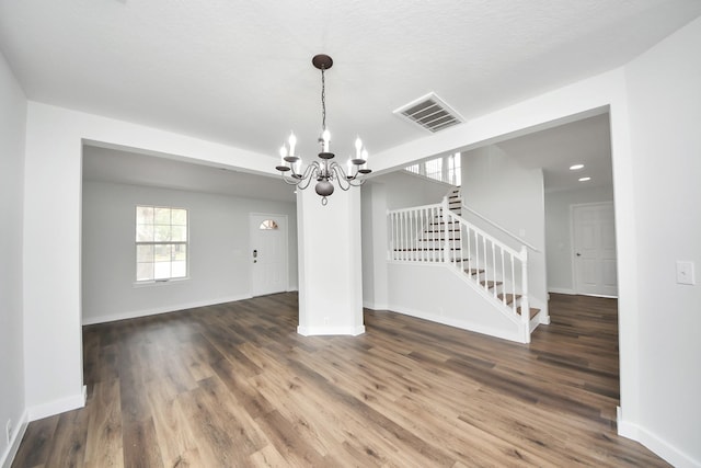 empty room with dark wood-style flooring, visible vents, baseboards, stairs, and an inviting chandelier