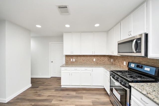 kitchen featuring visible vents, white cabinets, stainless steel appliances, light wood-style floors, and backsplash