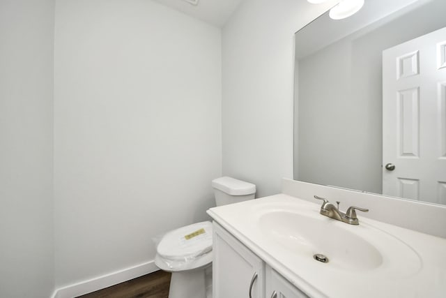 half bathroom featuring wood finished floors, vanity, toilet, and baseboards