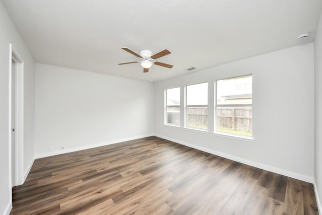 empty room with dark wood-type flooring, visible vents, and baseboards