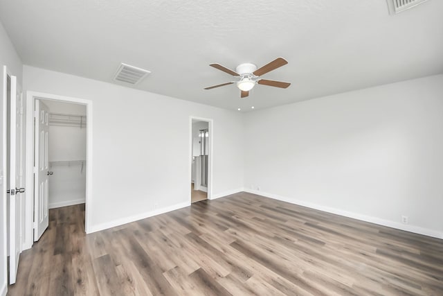 unfurnished bedroom featuring dark wood-style floors, visible vents, a spacious closet, and baseboards