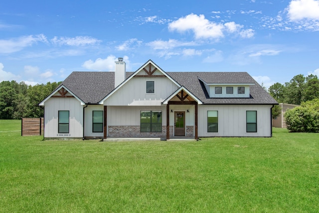 view of front of house with a chimney, brick siding, roof with shingles, and a front yard