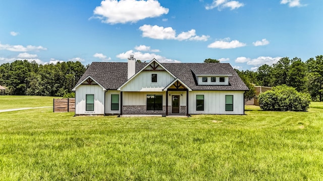 view of front of home featuring a shingled roof, a chimney, a front yard, and brick siding