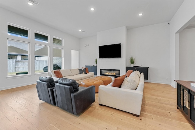 living area with light wood-type flooring, recessed lighting, baseboards, and a glass covered fireplace