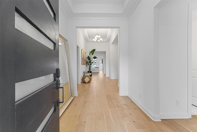 corridor with light wood-style floors, a raised ceiling, baseboards, and an inviting chandelier