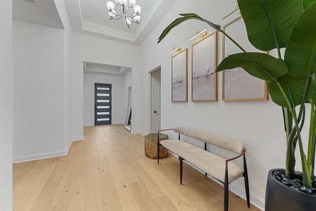 interior space with a chandelier, baseboards, a raised ceiling, and light wood-style floors