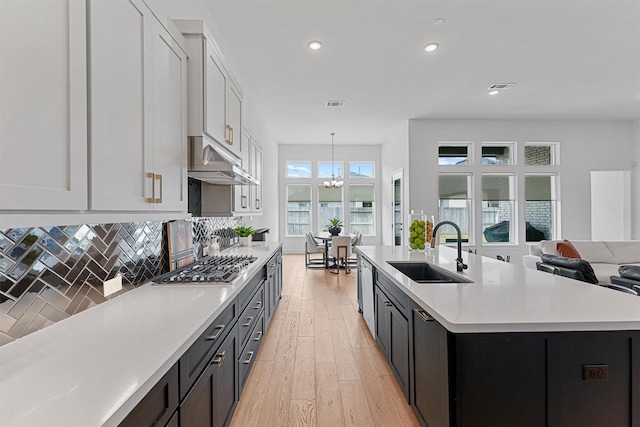 kitchen featuring light countertops, white cabinets, a sink, an island with sink, and under cabinet range hood