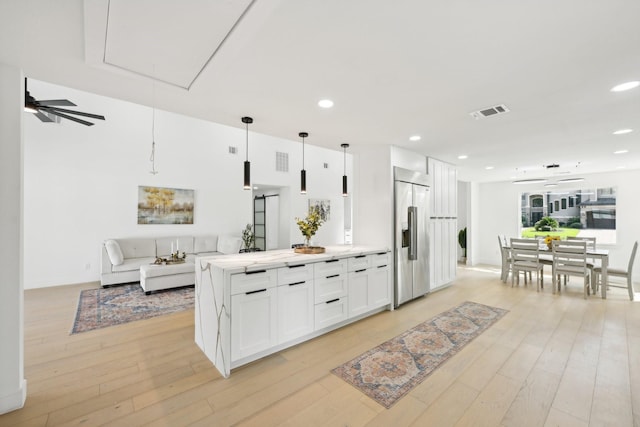 kitchen with built in refrigerator, white cabinetry, open floor plan, light countertops, and pendant lighting