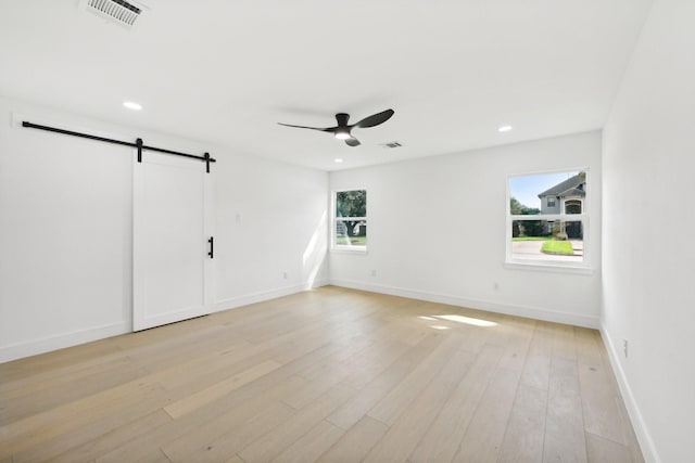 unfurnished room featuring light wood finished floors, recessed lighting, visible vents, a barn door, and baseboards