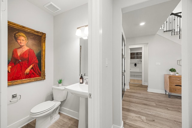 half bath with toilet, wood finished floors, visible vents, and baseboards