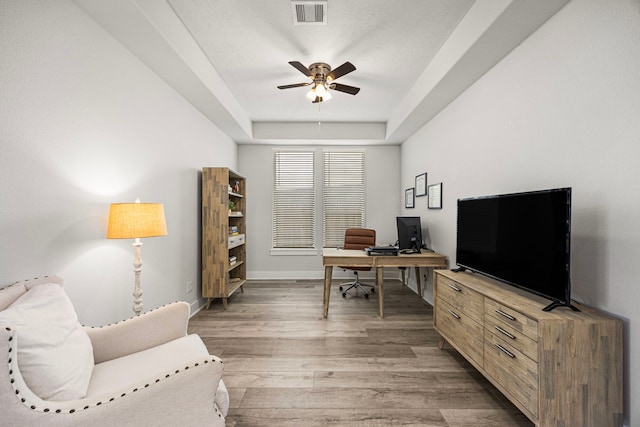 office area featuring baseboards, visible vents, a ceiling fan, a raised ceiling, and wood finished floors