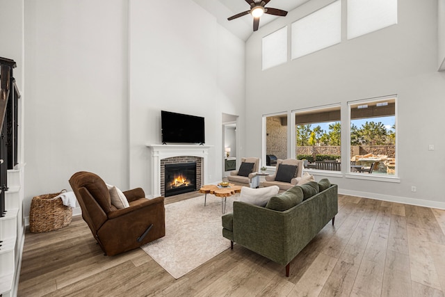 living area with a ceiling fan, light wood-type flooring, a fireplace, and baseboards