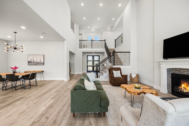 living area featuring a tile fireplace, light wood-style flooring, a high ceiling, baseboards, and stairs