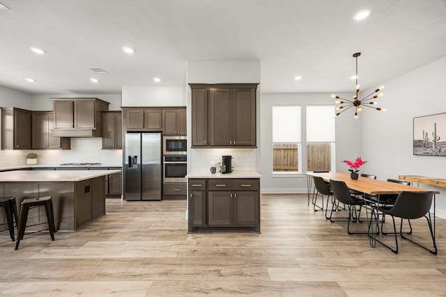 kitchen with a breakfast bar, pendant lighting, light countertops, appliances with stainless steel finishes, and dark brown cabinets