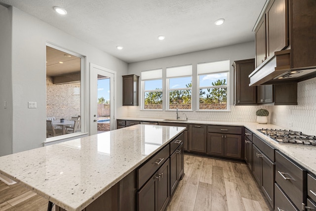 kitchen with light stone counters, a kitchen island, a sink, and stainless steel gas stovetop