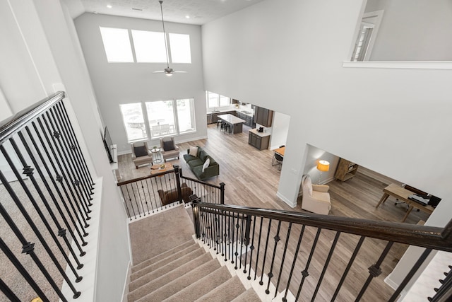 stairway with recessed lighting, a high ceiling, ceiling fan, wood finished floors, and baseboards