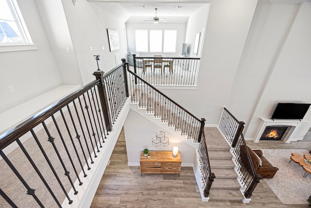 staircase with a high ceiling, wood finished floors, and a glass covered fireplace