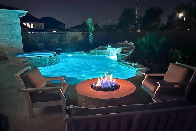 pool at night featuring an outdoor fire pit, a pool with connected hot tub, and fence