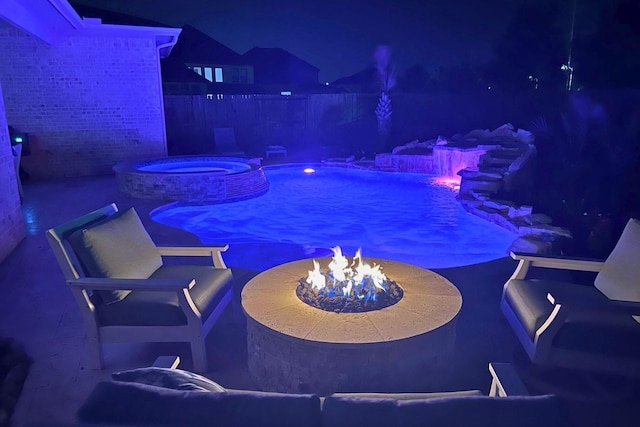 pool at night featuring a pool with connected hot tub and a fire pit