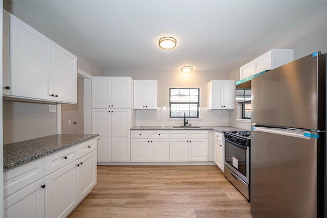 kitchen featuring appliances with stainless steel finishes, a sink, white cabinetry, and light stone countertops