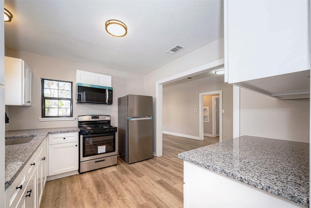 kitchen with light stone counters, stainless steel appliances, visible vents, light wood-style flooring, and white cabinets