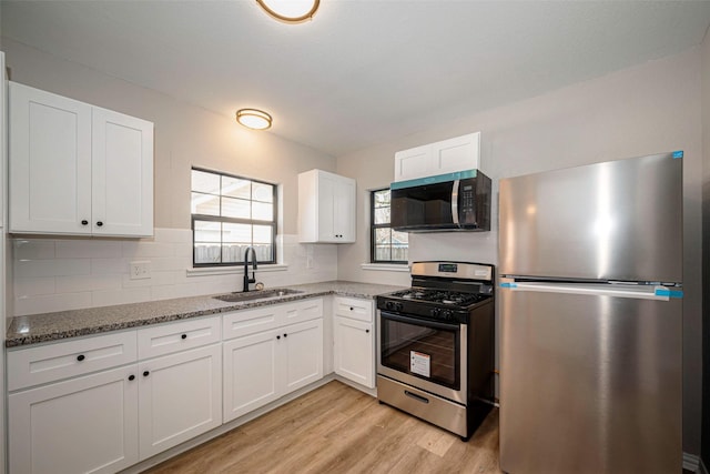 kitchen featuring dark stone countertops, appliances with stainless steel finishes, white cabinets, and a sink