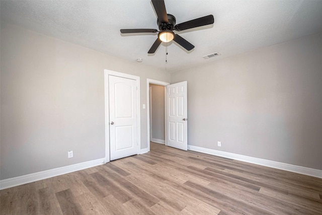 spare room with light wood-style flooring, a ceiling fan, visible vents, and baseboards