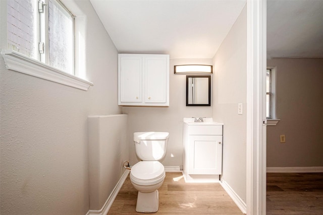 half bath with toilet, vanity, baseboards, and wood finished floors