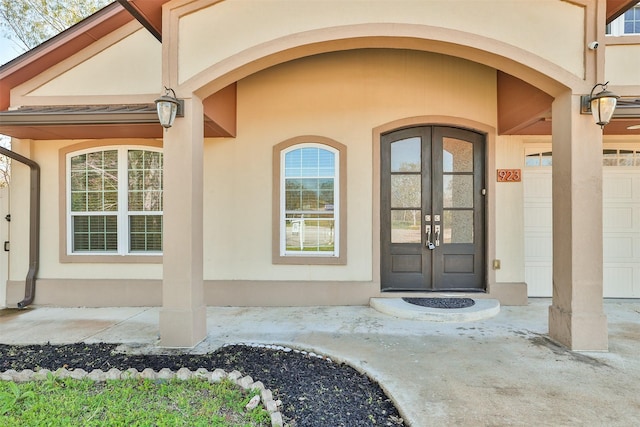 doorway to property with a garage, french doors, and stucco siding