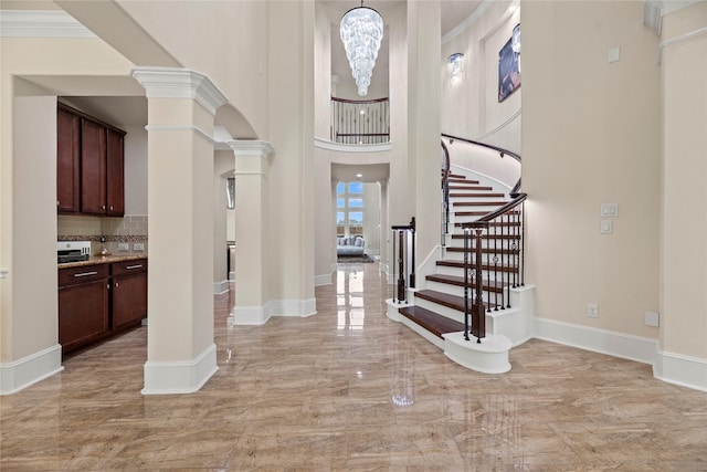 foyer featuring baseboards, marble finish floor, crown molding, and ornate columns