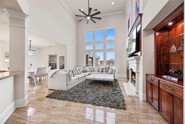 living area featuring ceiling fan, baseboards, a lit fireplace, decorative columns, and crown molding